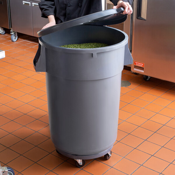 A person holding a large grey 44 gallon ingredient storage container with a lid.
