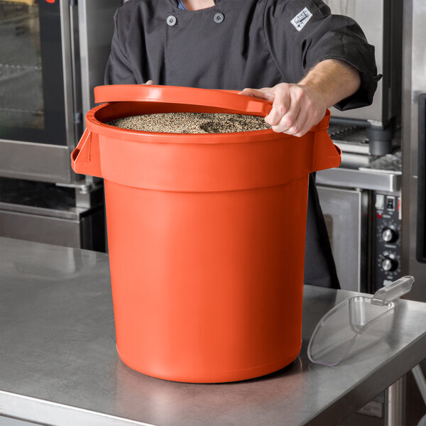 A man in a chef's uniform holding a large orange round ingredient storage bin.