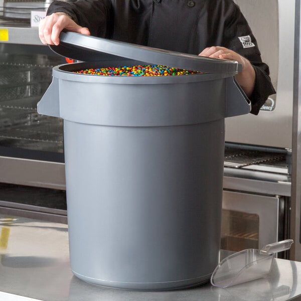 A man in a chef's uniform opening a large gray round ingredient storage bin.