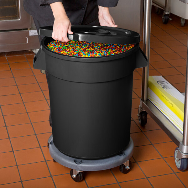 A woman using a black Mobile Ingredient Storage Bin to pour colorful candy on a counter.