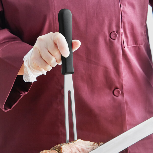A person holding a Mercer Culinary Millennia Pot Fork and a knife over a piece of meat.