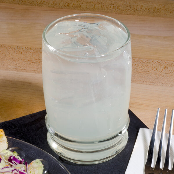 A Libbey water glass filled with ice water on a table with a plate of food and a fork and knife.