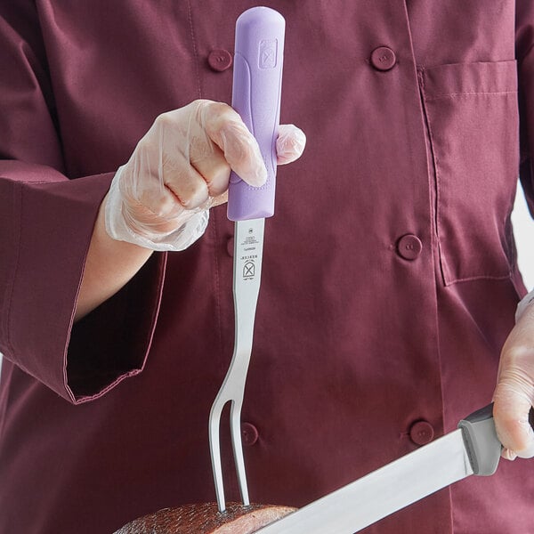 A person in a chef's uniform holding a Mercer Culinary Millennia pot fork with a purple handle.