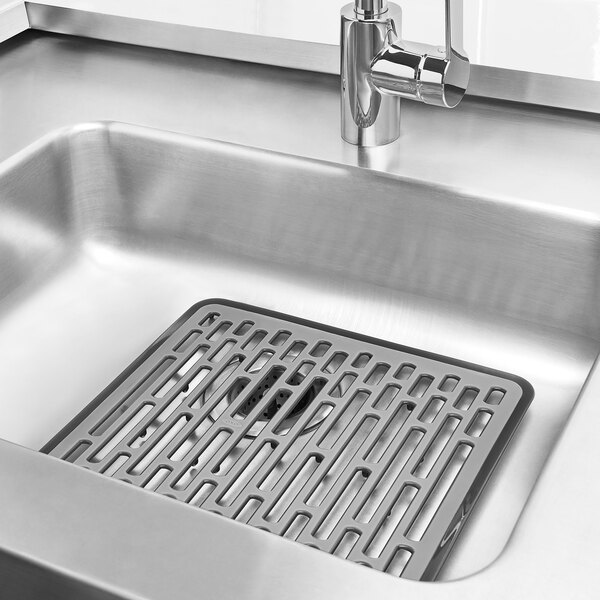 An OXO Good Grips plastic sink mat in a sink with a drain.