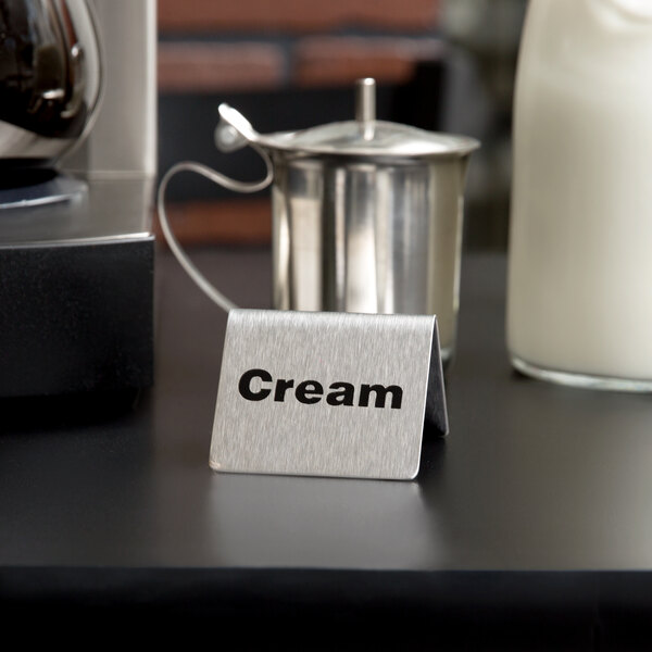 A stainless steel Tablecraft "Cream" tent sign on a hotel buffet table.