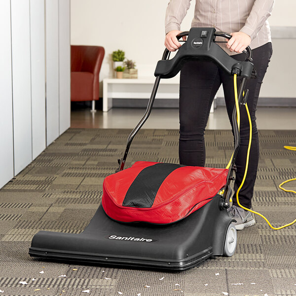A woman using a Sanitaire wide area vacuum cleaner in a corporate office cafeteria.