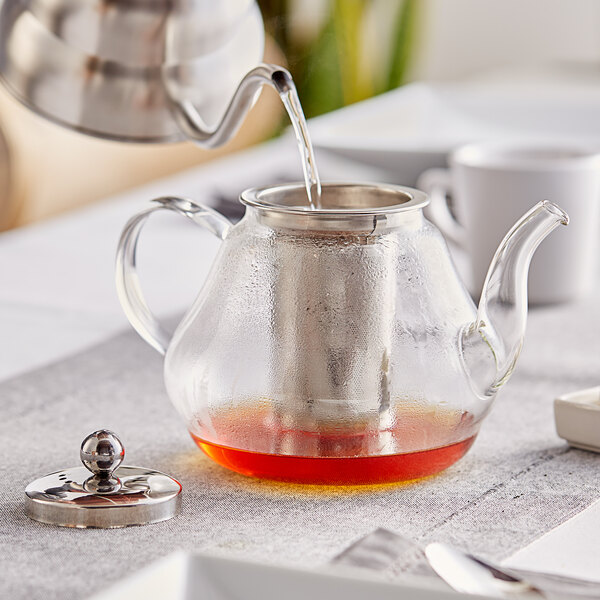A glass teapot with liquid being poured into it.
