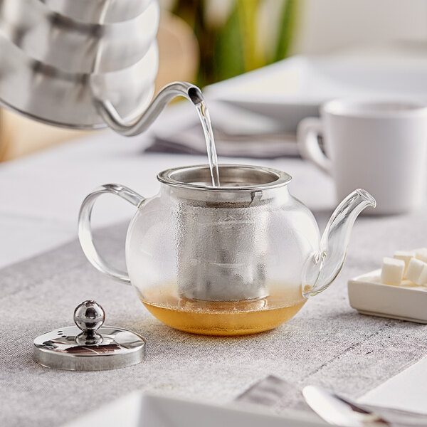 An Acopa glass teapot with a stainless steel infuser being poured into.