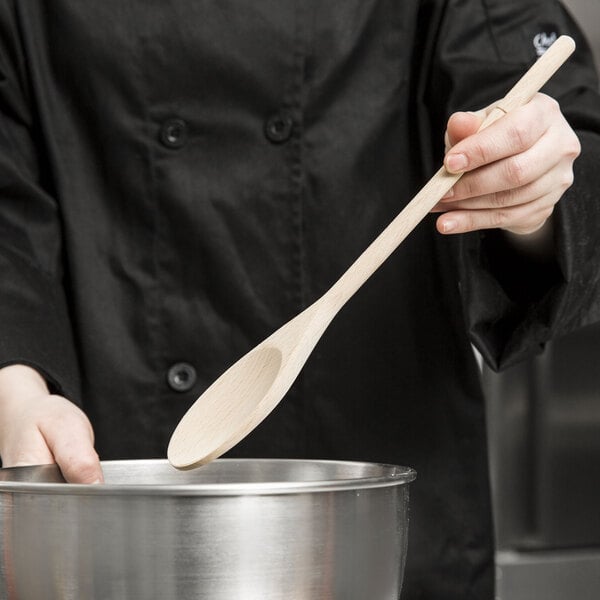 A person stirring a bowl with a Tablecraft beechwood wooden spoon.