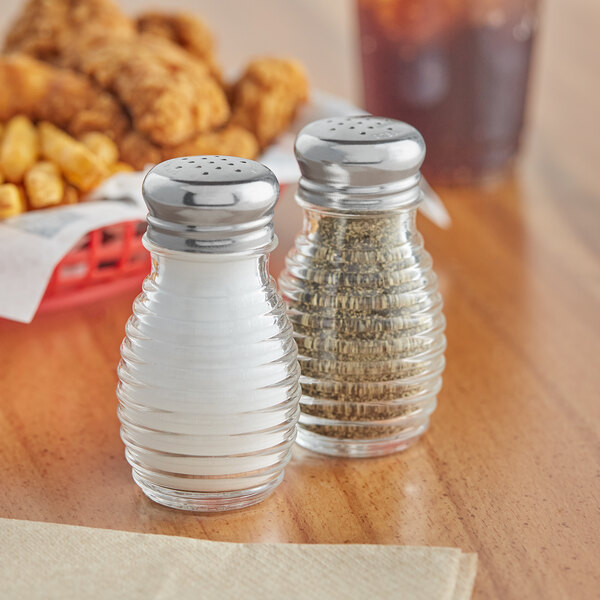 Two Tablecraft glass salt and pepper shakers with stainless steel tops on a table.