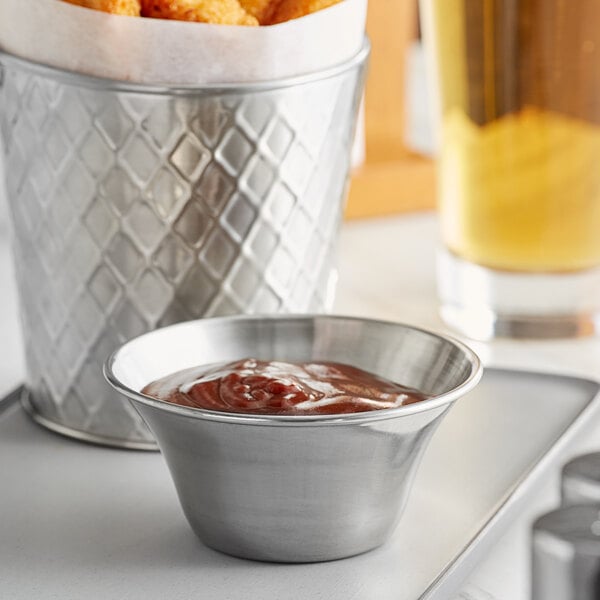 A Tablecraft stainless steel sauce cup filled with sauce on a table.