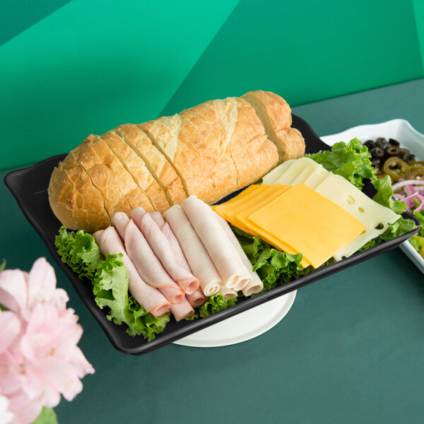A black scalloped melamine rectangular display tray with food on a table.
