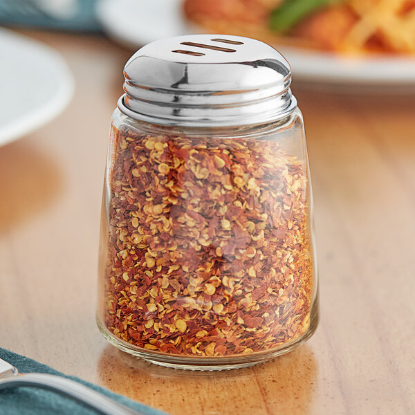 A Tablecraft glass cheese shaker with a chrome-plated slotted top filled with crushed red pepper flakes.