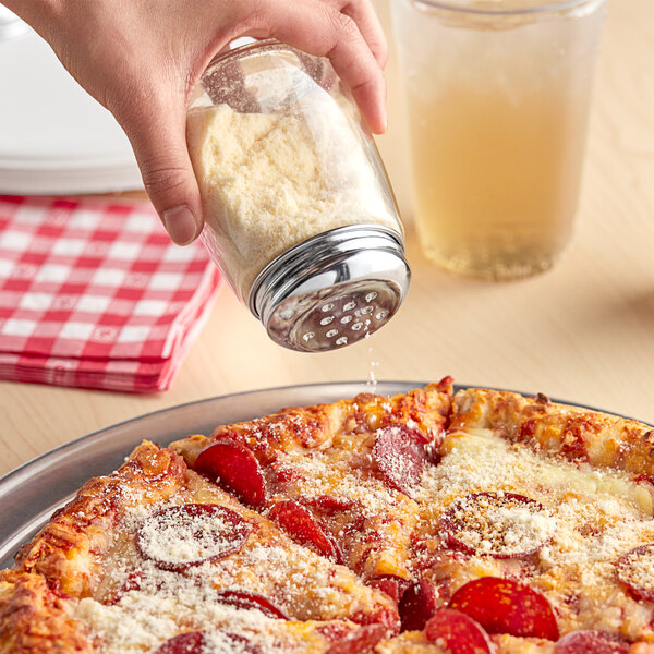 A hand using a Tablecraft modern glass cheese shaker to sprinkle cheese on a pepperoni pizza.