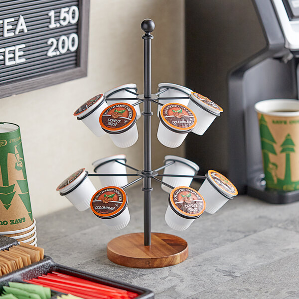 A Tablecraft black steel and wood 2-tier coffee cone and K-cup holder filled with a variety of coffee cups.