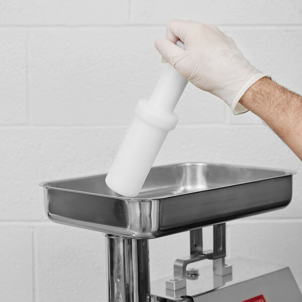 A person in a white glove using an Avantco plastic pusher to grind meat.