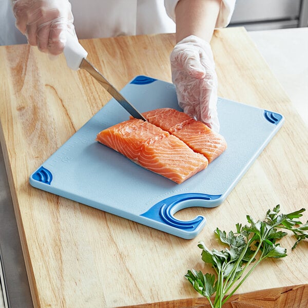 A person using a San Jamar blue cutting board to cut salmon.