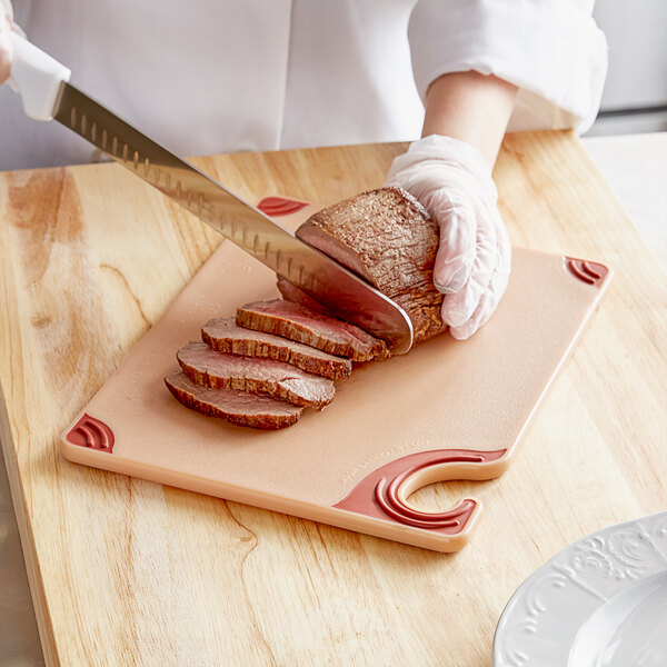 A person cutting meat on a San Jamar brown cutting board.