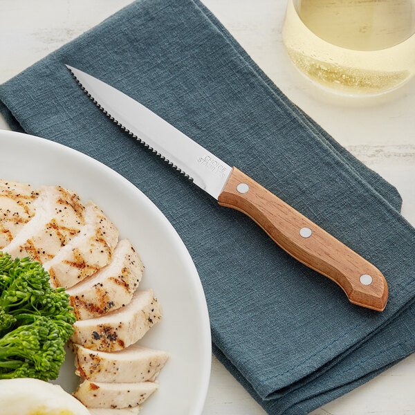 A Choice steak knife with a light brown wood handle on a white plate with chicken and broccoli.