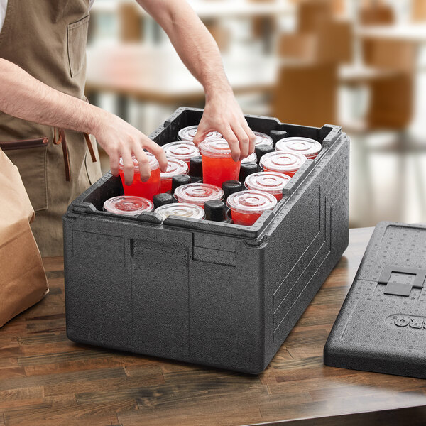 A man putting cups in a Cambro Cam GoBox food pan carrier with cup holders.