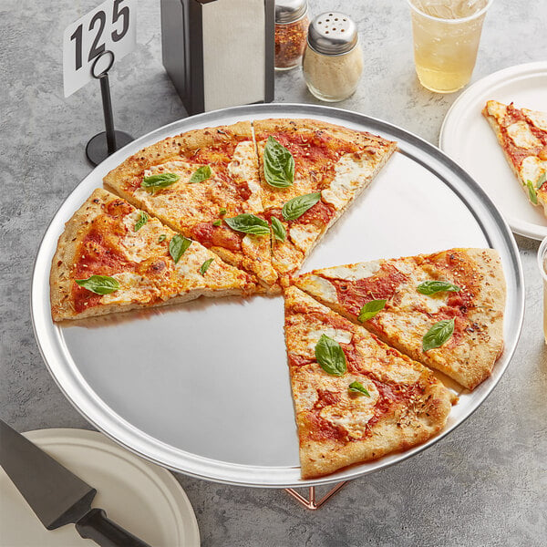 An 18" wide rim aluminum pizza pan with slices of pizza, some with basil leaves on top.