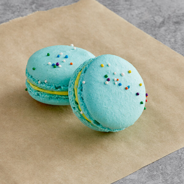 Two blue Macaron Centrale with sprinkles on a brown surface.
