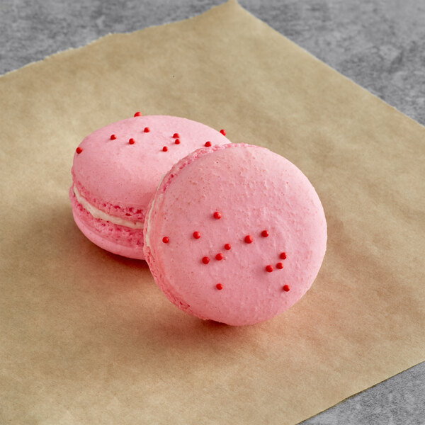 Two pink Pomegranate Macarons on brown paper.