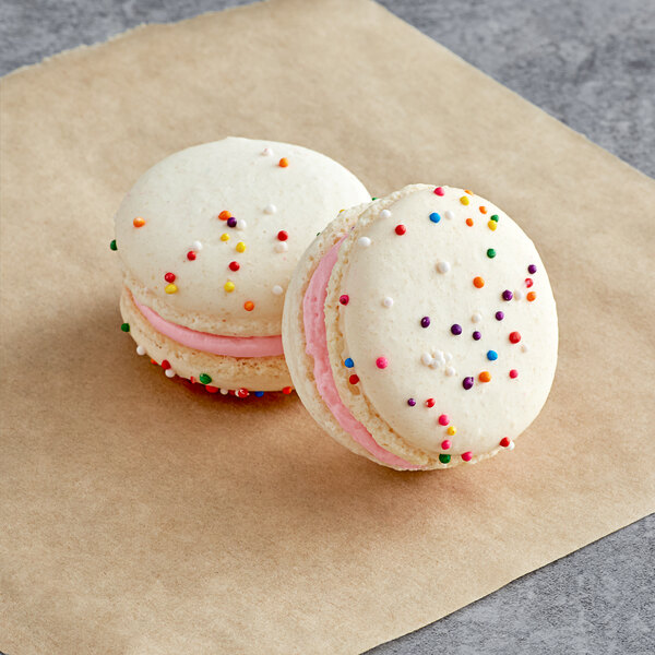 Two Macaron Centrale birthday cake macarons with white cookies and sprinkles on top.