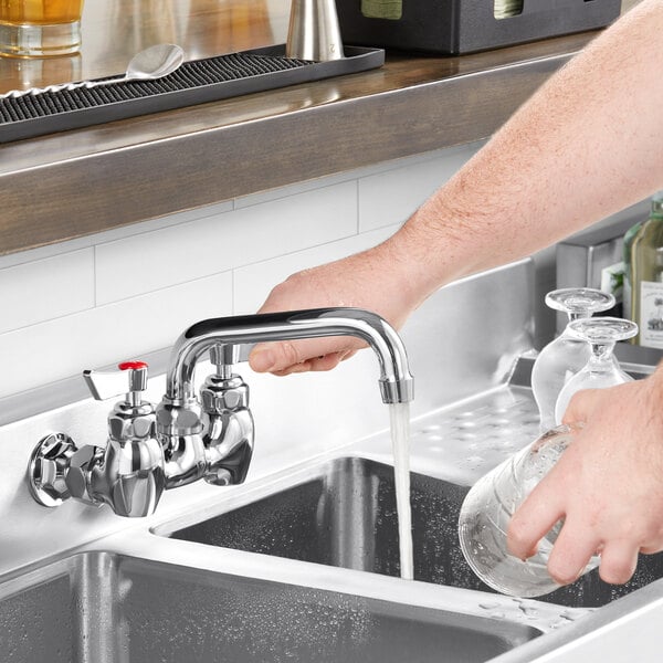 A person using a Waterloo wall-mounted faucet to pour water into a sink.