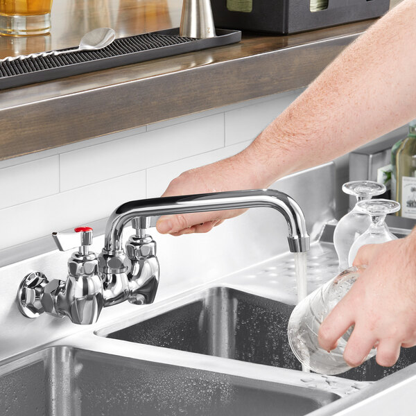 A hand pouring water from a Waterloo wall-mounted faucet over a sink.