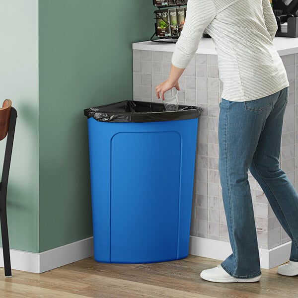 A woman putting a plastic bag into a blue Lavex corner round trash can.