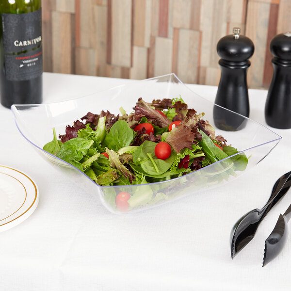 A clear Fineline plastic serving bowl filled with salad with tomatoes and lettuce.