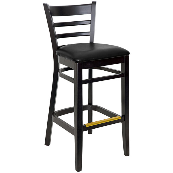 A BFM Seating black beechwood ladder back barstool with a black cushioned seat.