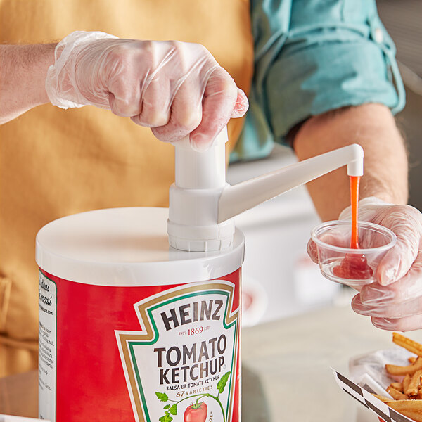 A person using a Choice plastic condiment pump to pour red liquid into a container.