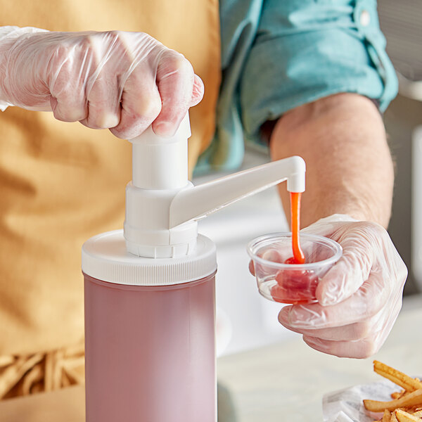 A person in gloves using a Choice condiment pump to pour sauce into a plastic container.