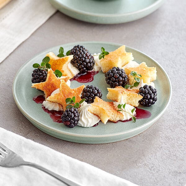 An Acopa Pangea porcelain plate with a star shaped pastry with cream and berries on it.