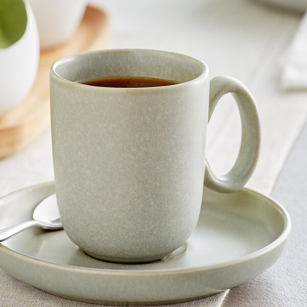 An Acopa Pangea porcelain cup of coffee on a saucer with a spoon on a table.