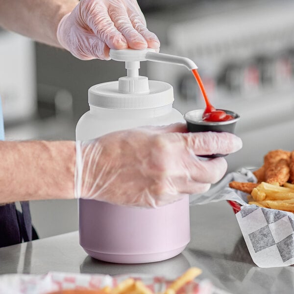 A person in gloves using a white plastic pump to pour ketchup into a container.