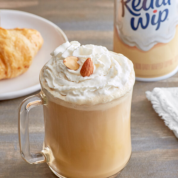 A glass mug of coffee with Reddi-Wip almond milk whipped topping and almonds.