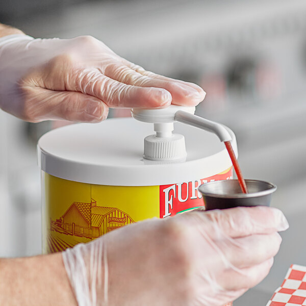 A person in gloves using a Choice condiment pump to pump liquid into a container.