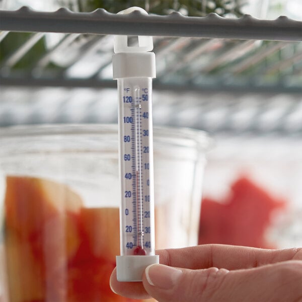 A hand holding a Miljoco refrigerator/freezer thermometer.