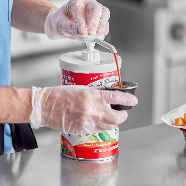A person in gloves using a Choice condiment pump to pour sauce into a container with a red lid.