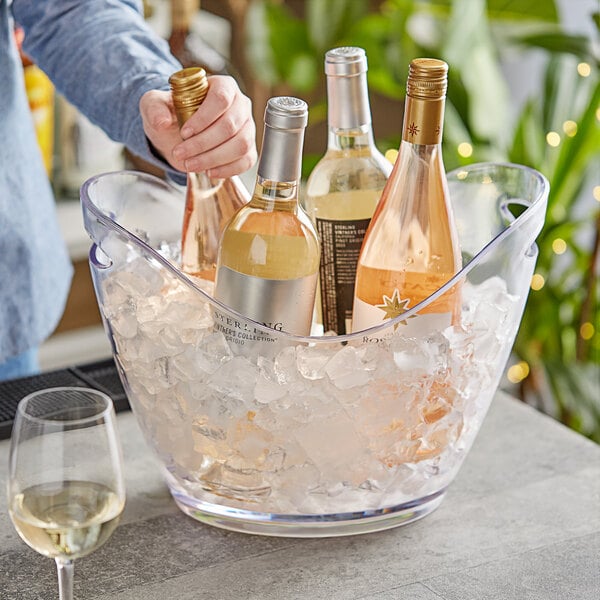 A person pouring white wine into a Choice plastic wine bucket with ice on a table in a winery cellar.