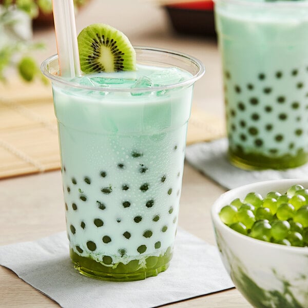 A glass of bubble tea with a straw and kiwi popping boba in it.