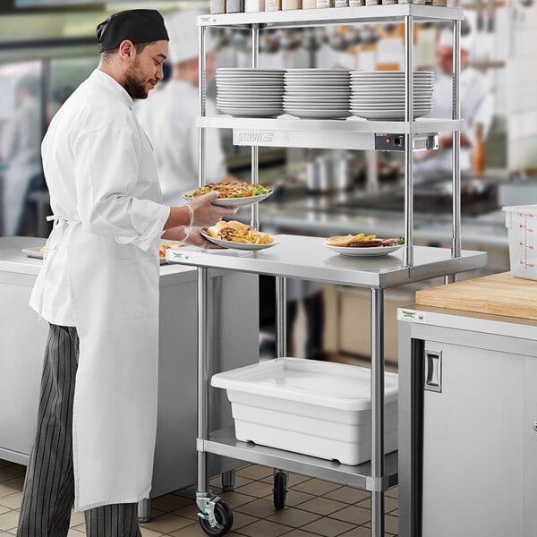 A man in a white coat using a Regency expeditor table to hold food plates.