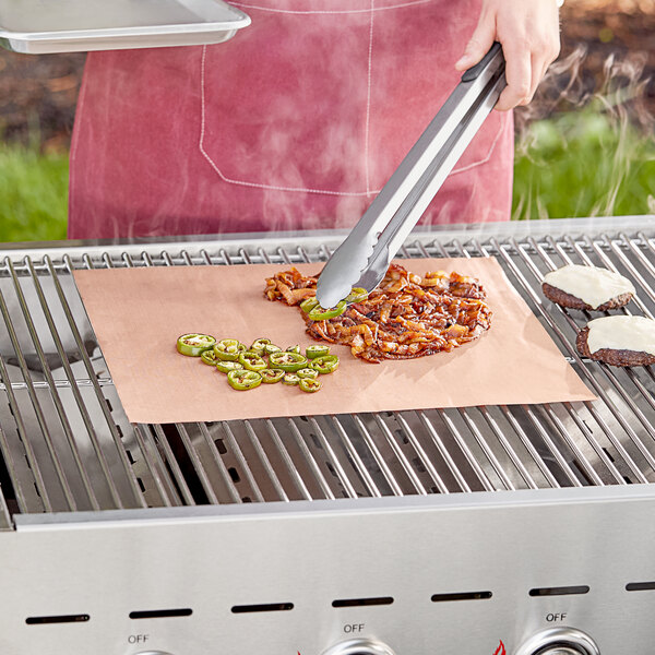 A person using a Mr. Bar-B-Q non-stick copper grill mat to cook food on a grill.