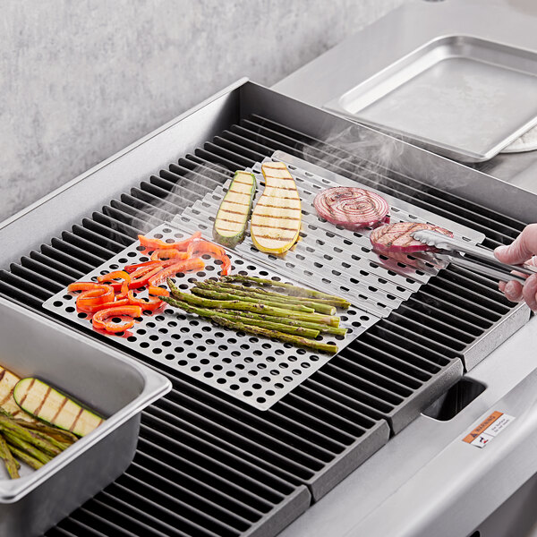 A person using Mr. Bar-B-Q stainless steel grill sheet to cook vegetables on a grill.