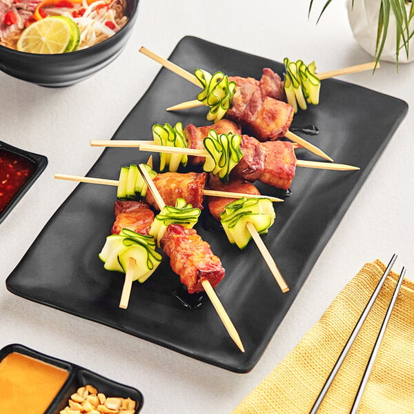 A black Acopa Izumi melamine platter with skewers and a bowl of food on a table.