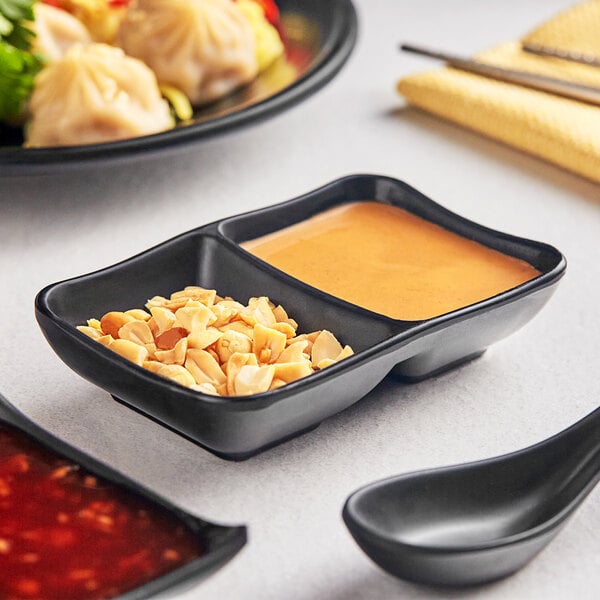 An Acopa Izumi matte black melamine sauce dish with two compartments, one with sauce and peanuts.