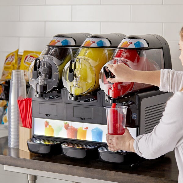 A woman pouring a red frozen beverage from a Vollrath machine into a cup.
